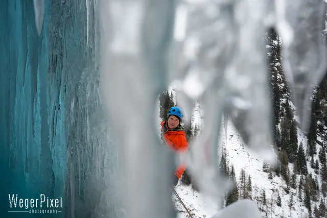 Eiskletterer mit blauem Helm, fotografiert durch einen Vorhang aus Eiszapfen