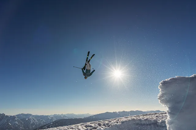Freeskier im Rückwärtssalto vor der Sonne über einer verschneiten Wechte
