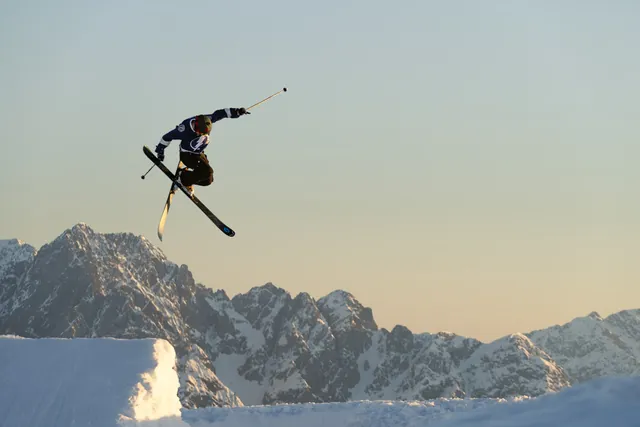 Skifahrer im Sprung über einer Schneekante, dahinter schroffe Felsgipfel im Abendlicht