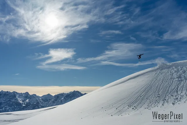 Freeskierin hoch in der Luft über einem Schneehang am Zettersfeld, Sonne zwischen Wolken