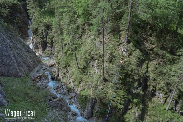 Highline über einer bewaldeten Schlucht mit Wildbach