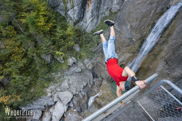 Athlet macht eine Human Flag an einem Geländer über dem Wasserfall Frauenbach in Lavant