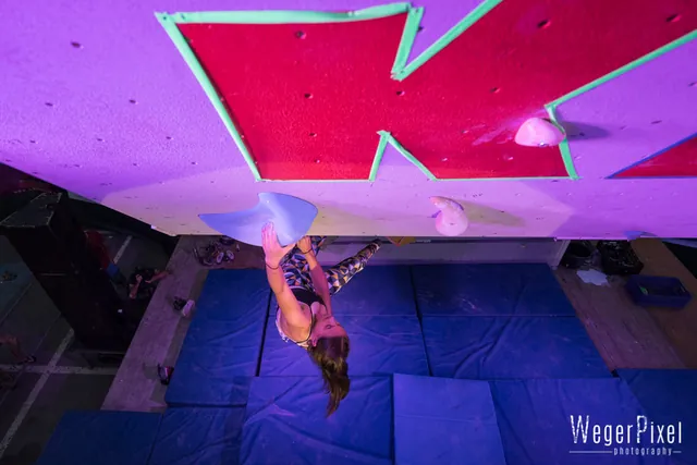 Kletterer hängt kopfüber im bunt beleuchteten Boulderdach beim KIOT Bouldercup
