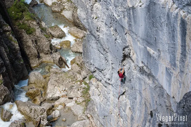 Kletterer in einer steilen Felswand, schräg von oben fotografiert, unten rauscht der Bach