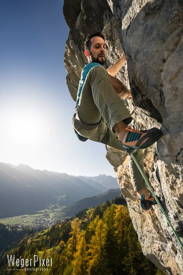 Kletterer hängt im Überhang im Gegenlicht, darunter das Tal