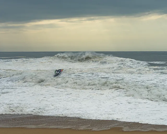 Jetski in der weißen Brandung vor Nazaré, Sonnenstrahlen brechen durch die Wolken