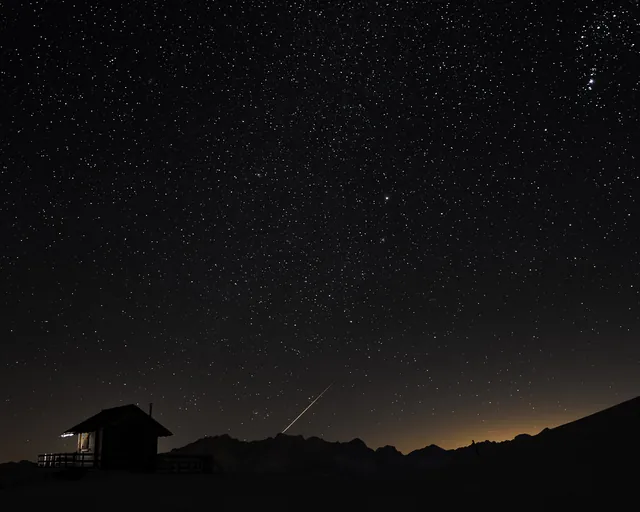 Sternenhimmel mit Sternschnuppe über einer Hütte am Zettersfeld in Osttirol im Winter